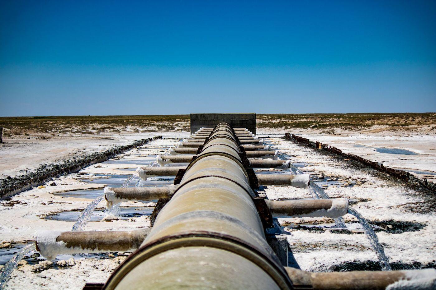 An industrial pipeline discharging water across dry ground beside a treatment site