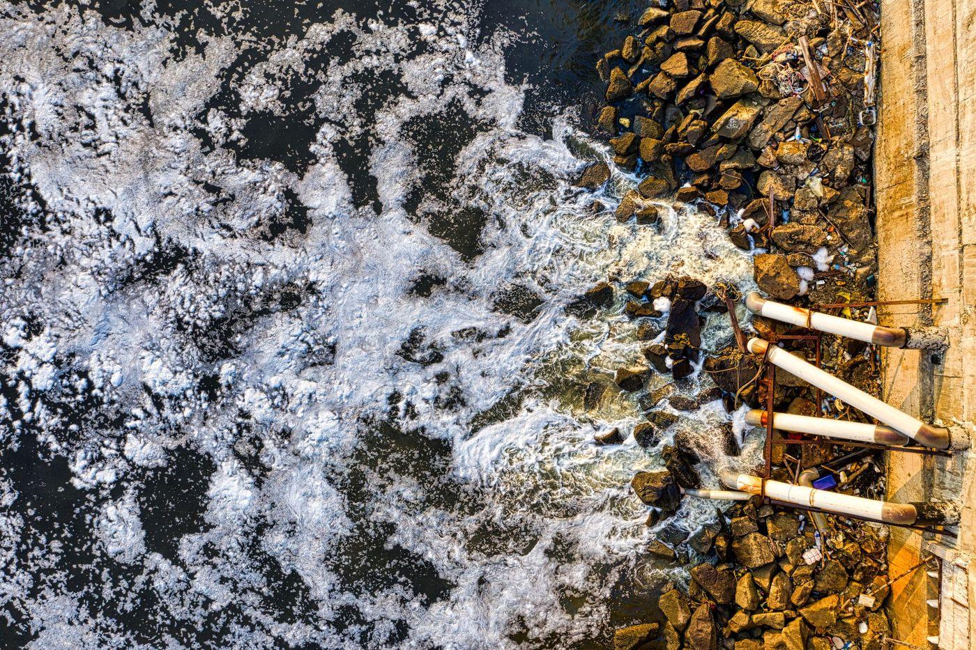 Foam-streaked discharge water spreading out from an outfall beside a rocky breakwater